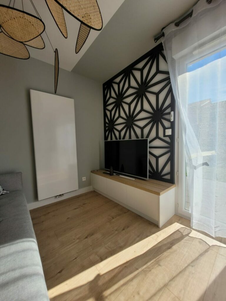 L'image montre un joli meuble télé couleur blanc et bois ainsi qu'un claustra décoratif de couleur sombre